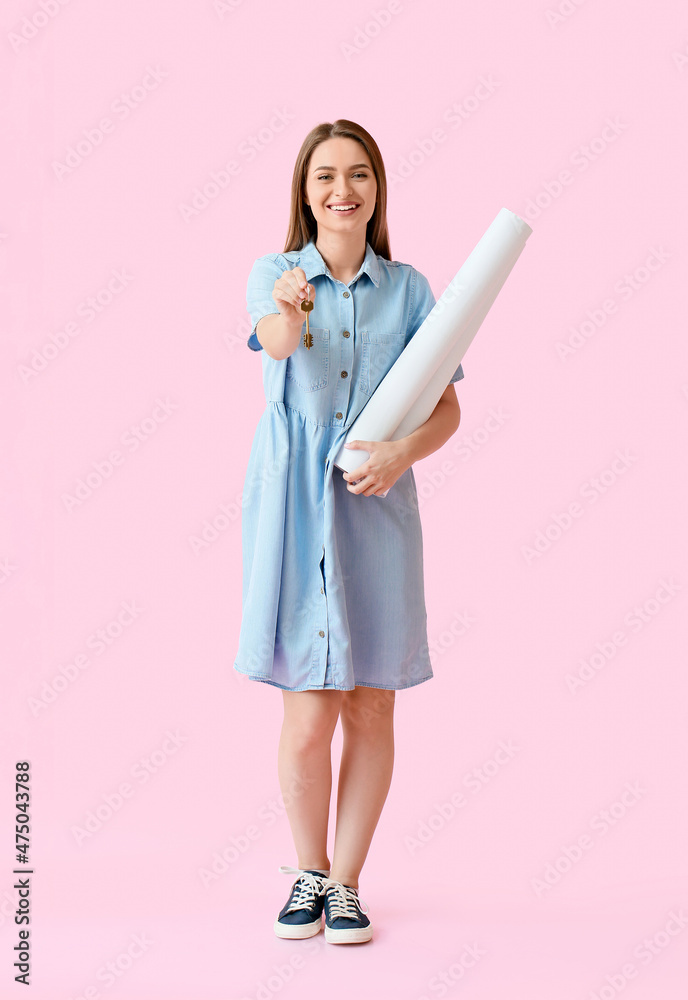 Smiling young woman with key from house and rolls of paper on pink background Smiling young woman with key from house and rolls of paper on pink background