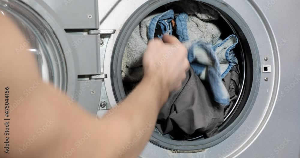 Man puts dirty things in an automatic washing machine. Mens hands load the washing machine with dirty laundry and clothes. Concept of washing at home, everyday life, household chores, homework Man puts dirty things in an automatic washing machine. Mens hands load the washing machine with dirty laundry and clothes. Concept of washing at home, everyday life, household chores, homework
