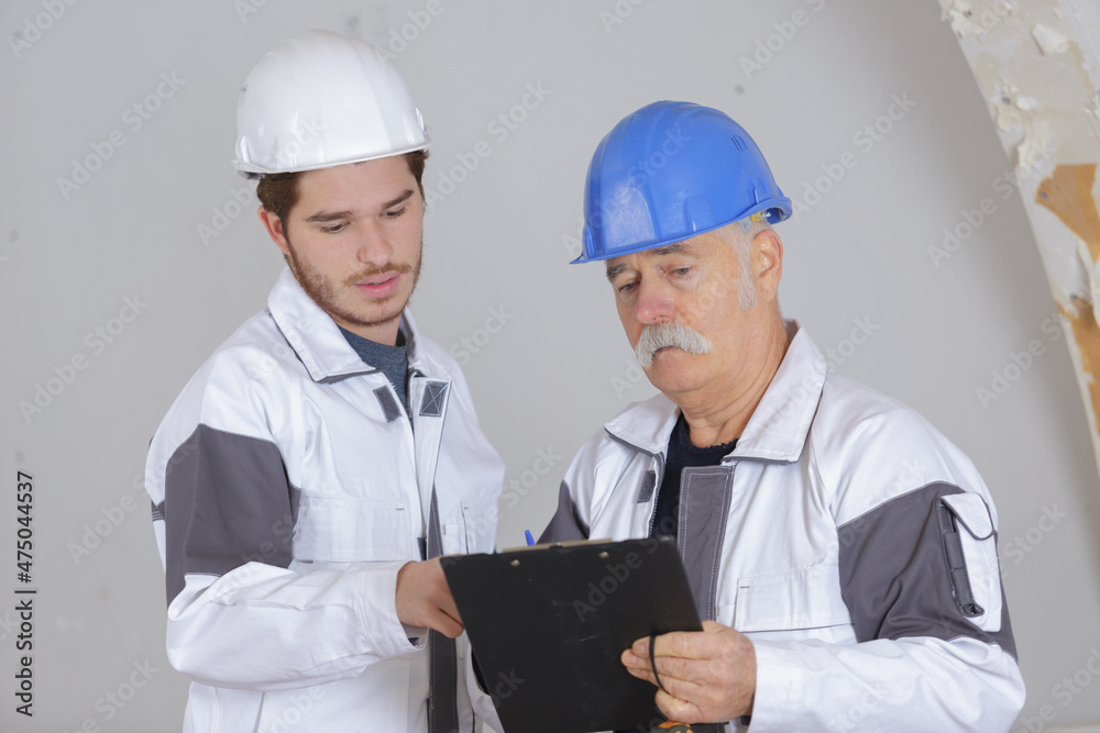 senior builder holding clipboard with younger builder senior builder holding clipboard with younger builder