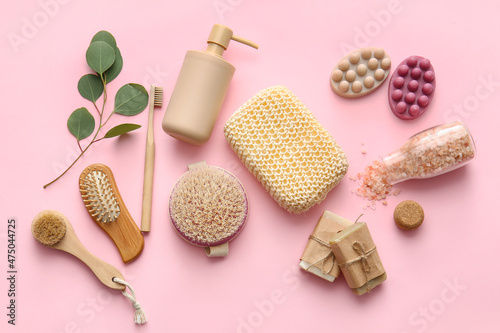 Set of bath supplies with loofah sponge and plant branch on pink background