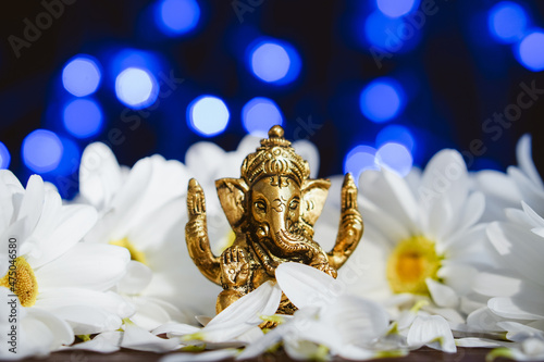 Golden lord ganesha sculpture in daisy flowers over blue illuminated background. Celebrate lord ganesha festival photo