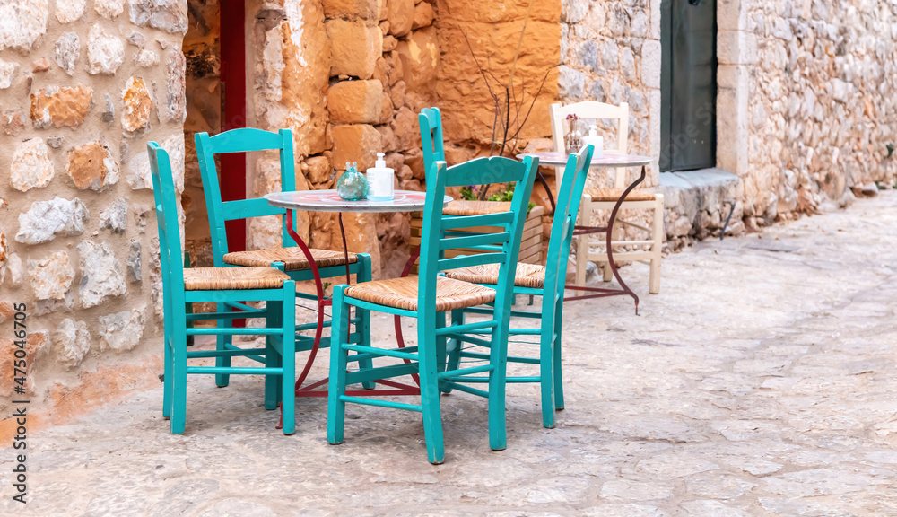 Open air cafe bar. Empty seats on cobblestone street, stone wall background, Areopoli, Mani Greece