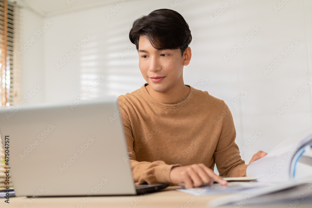 Entrepreneur handsome business asian man wear casual shirt working with laptop and look at document to compare something at home.Happy Attractive Freelance smart working online enjoy with own business Entrepreneur handsome business asian man wear casual shirt working with laptop and look at document to compare something at home.Happy Attractive Freelance smart working online enjoy with own business