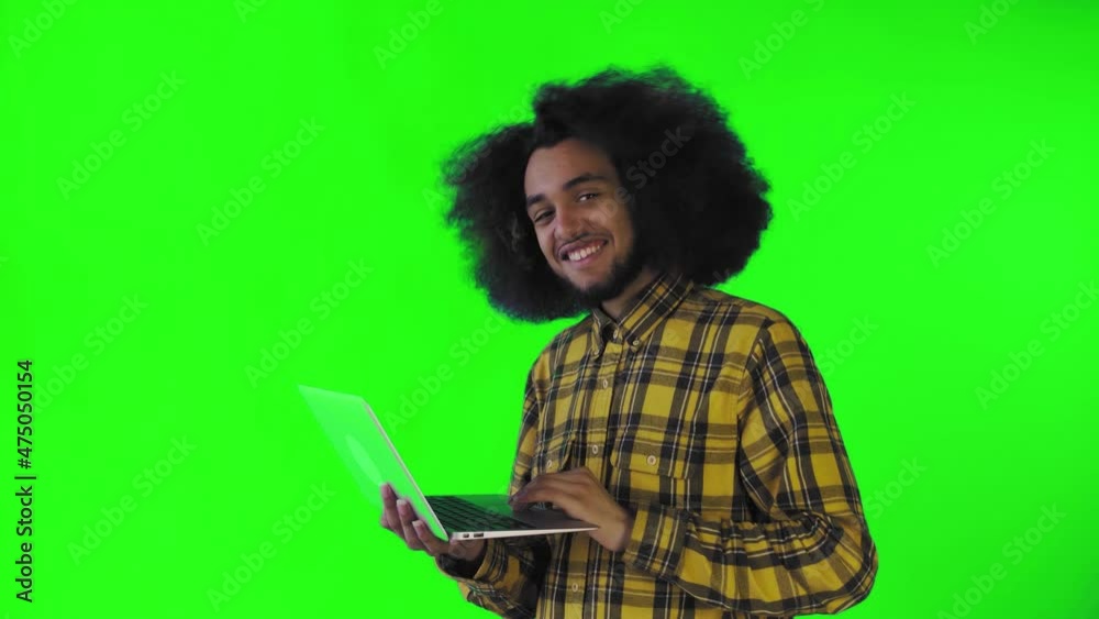 A young man with an African hairstyle on a green background is typing on a laptop. On a colored background A young man with an African hairstyle on a green background is typing on a laptop. On a colored background