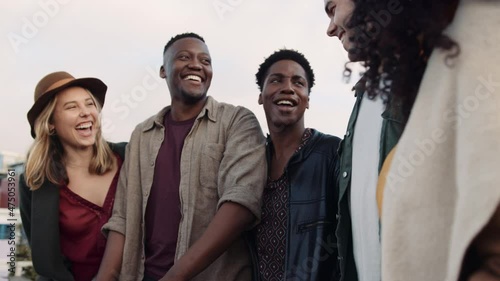 Multi-ethnic group of adult friends cheerfully socializing on a rooftop balcony in the city.