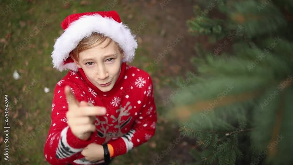 boy in a red knitted Christmas sweater with a Christmas reindeer and a Santa hat is unhappy and waving his finger at the camera boy in a red knitted Christmas sweater with a Christmas reindeer and a Santa hat is unhappy and waving his finger at the camera