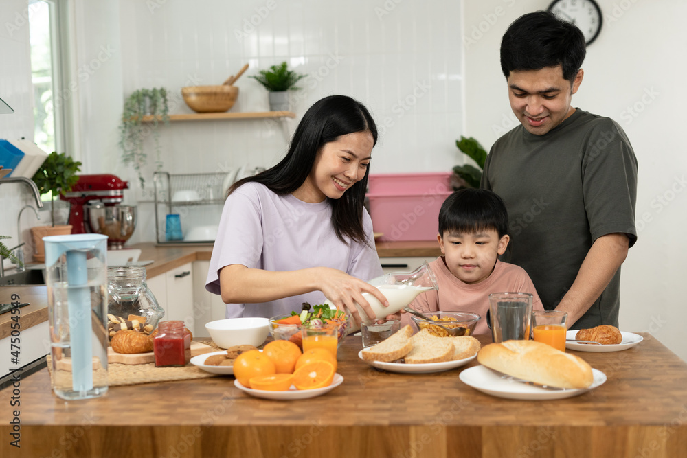 Asian family breakfast at home. Parents and children enjoy eating together, talking with laughter and good atmosphere. Father and mother plays with son playfully at kitchen table. Asian family breakfast at home. Parents and children enjoy eating together, talking with laughter and good atmosphere. Father and mother plays with son playfully at kitchen table.