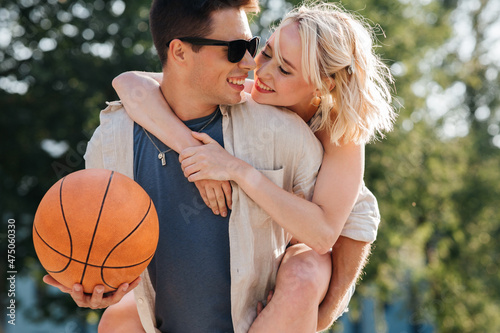 summer holidays, love and people concept - happy young couple with ball having fun on basketball playground