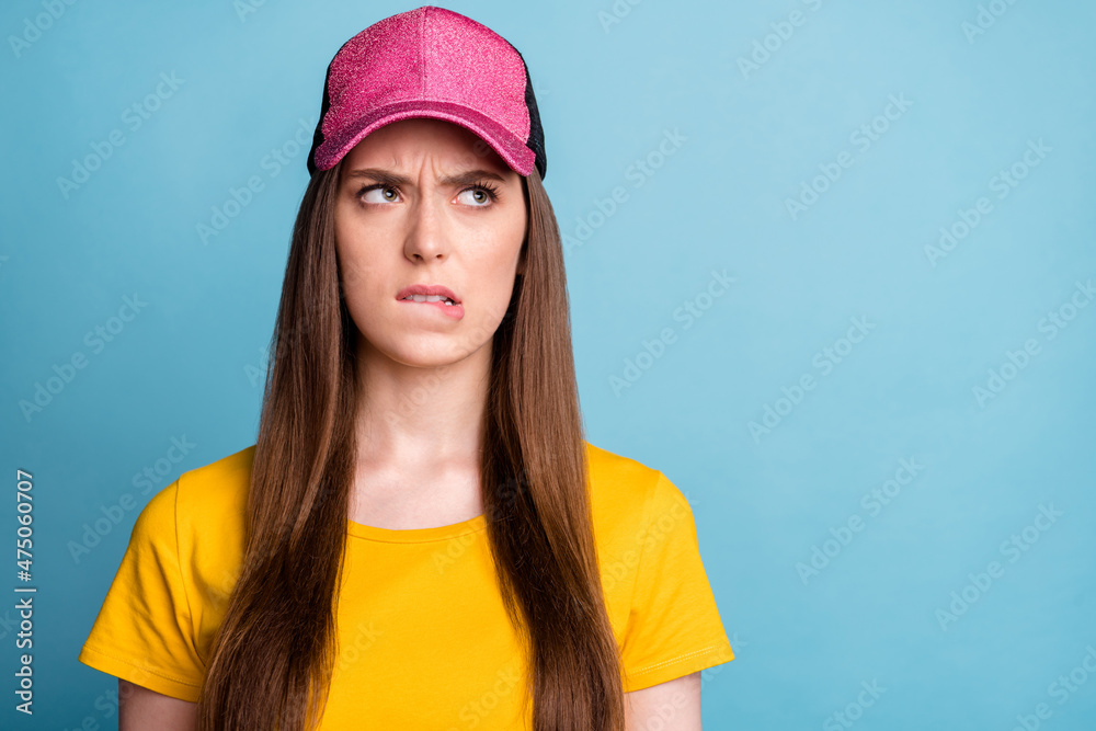 Photo of unsure upset jealous lady bite lip look empty space wear pink cap yellow t-shirt isolated blue color background