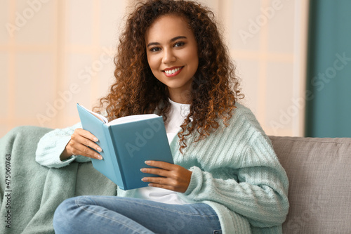 Young African-American woman in warm cardigan with book at home
