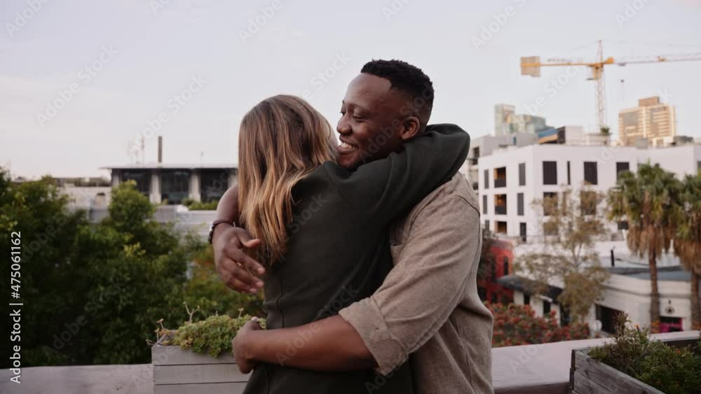 Caucasian female happily greeting black male friend at a rooftop party in the city at dusk Caucasian female happily greeting black male friend at a rooftop party in the city at dusk