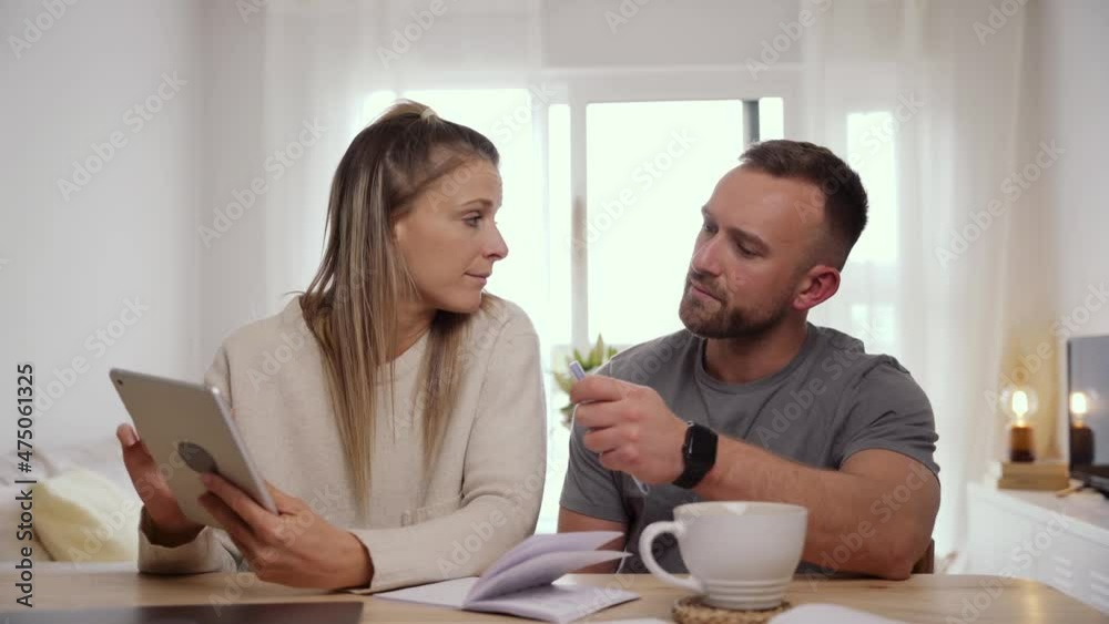 Caucasian couple sitting at home typing on digital tablet sorting out finances Caucasian couple sitting at home typing on digital tablet sorting out finances
