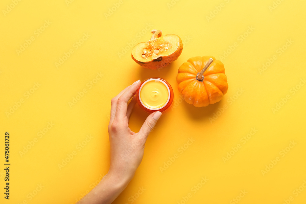 Female hand with jar of natural mask and ripe pumpkin on yellow background