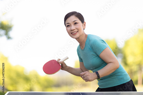 Happy mature woman playing table tennis outdoors