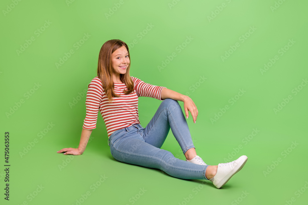 Photo of positive nice pretty lady sit floor enjoy rest wear striped shirt jeans isolated green color background Photo of positive nice pretty lady sit floor enjoy rest wear striped shirt jeans isolated green color background