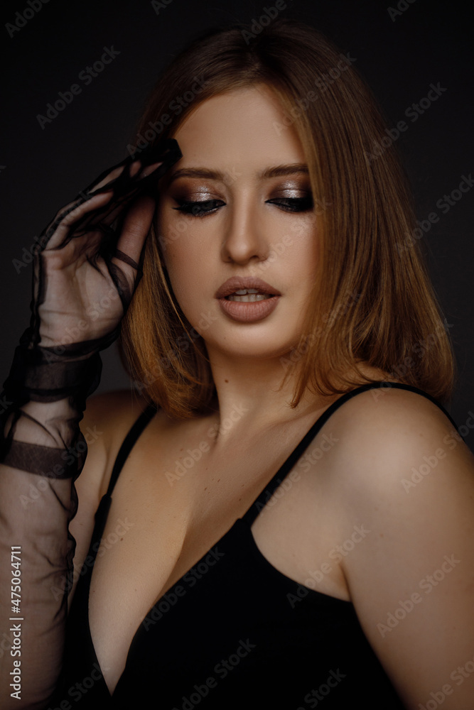 Caucasian woman on a gray background wearing a black evening dress and looking at the camera, stylish and beautiful Caucasian woman on a gray background wearing a black evening dress and looking at the camera, stylish and beautiful
