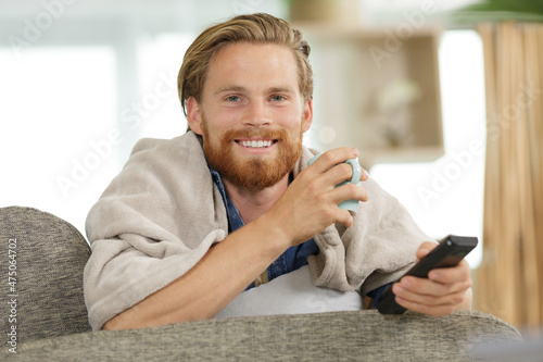 man under blanket on sofa with drink and remote control
