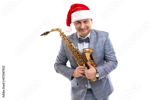 Funny musician wears in Santa s hat holds saxophone while showing thumb up on studio background