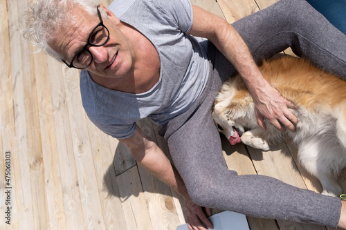 A smiling gray-haired man strokes a dog sitting on a sunny terrace