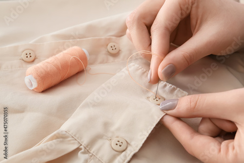 Woman sewing button on shirt sleeve, closeup