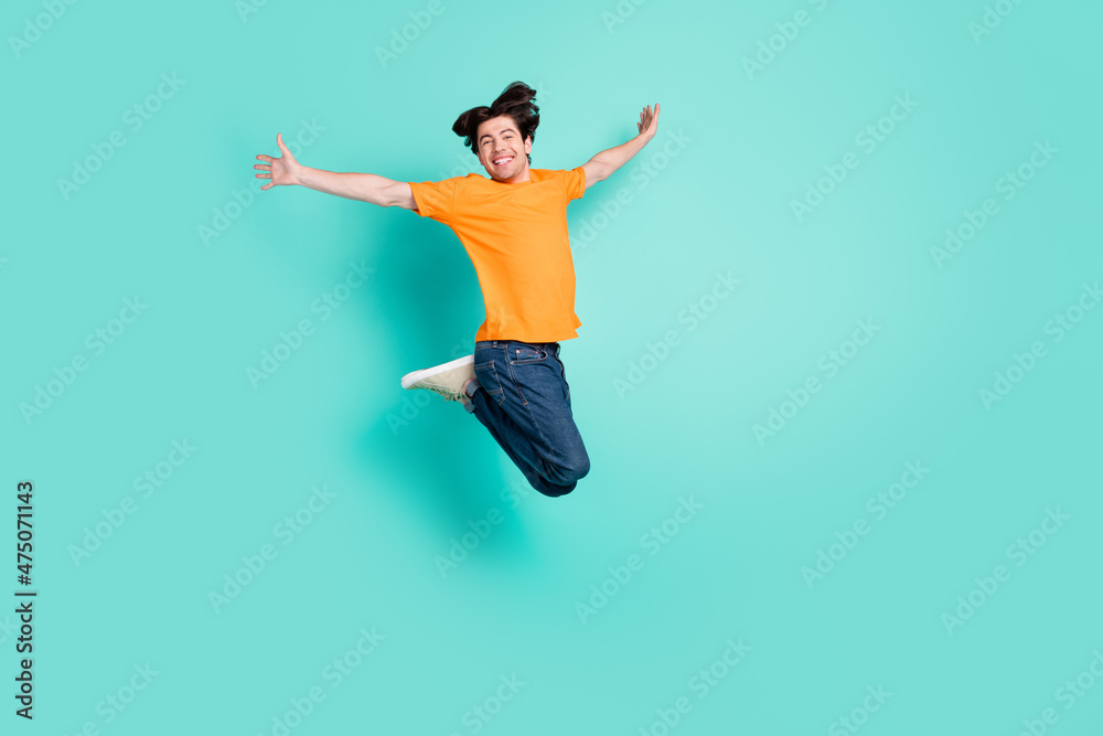 Full size photo of funny brown hair young guy jump wear t-shirt jeans sneakers isolated on blue background