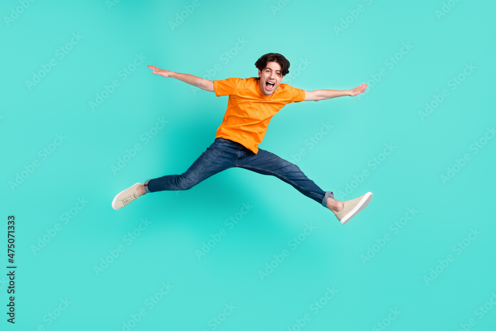 Full body photo of crazy brown hair millennial guy jump yell wear t-shirt jeans sneakers isolated on blue background