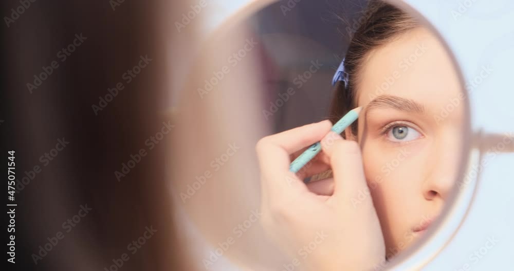 Selective focus. A young beautiful girl in front of the mirror paints her eyebrows with a special cosmetic pencil. The concept of self-care, cosmetologist, makeup at home. Close-up. 4K Selective focus. A young beautiful girl in front of the mirror paints her eyebrows with a special cosmetic pencil. The concept of self-care, cosmetologist, makeup at home. Close-up. 4K