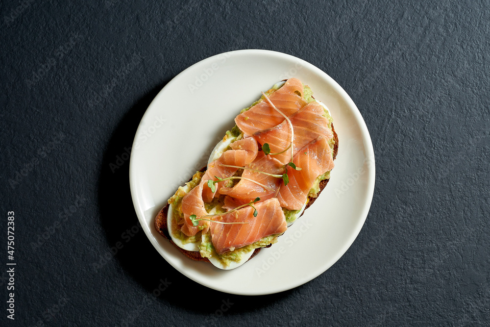 Toast with salmon and avocado mousse in a white plate on a black background Toast with salmon and avocado mousse in a white plate on a black background