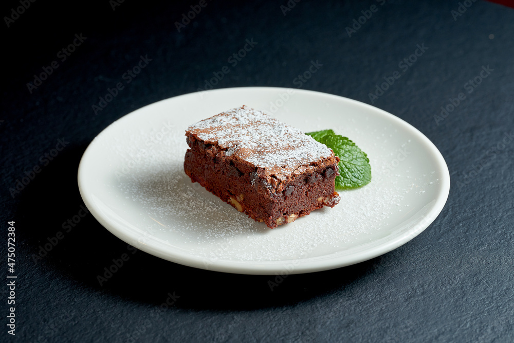 Brownie cake with nuts in a white plate on a dark background.