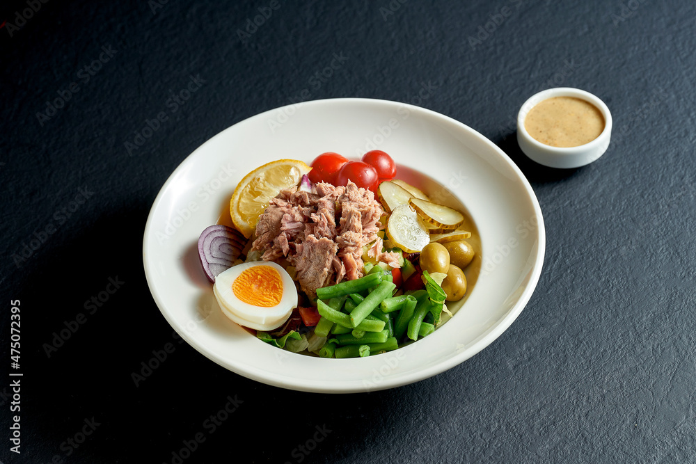 Diet nicoise salad with tuna, egg and asparagus in a white plate on a black background Diet nicoise salad with tuna, egg and asparagus in a white plate on a black background