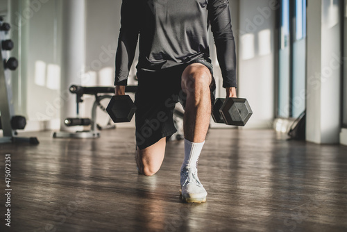 Young athlete holding dumbbells and exercising in the gym. He exercises to build muscle strength.