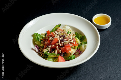 Diet salad with tomatoes and cucumbers, seeds in a white plate on a black background