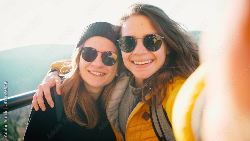 Two young women in sunglasses taking a selfie while standing on an observation deck against the blue sky on a sunny day. Two young women in sunglasses taking a selfie while standing on an observation deck against the blue sky on a sunny day.