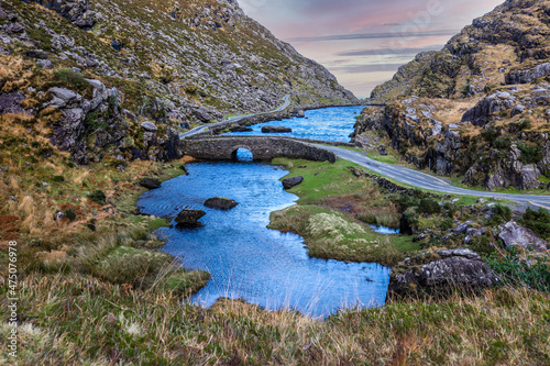 Stone Wishing Bridge over winding stream in green valley at Gap of Dunloe in Black Valley of Ring of Kerry, County Kerry, Ireland