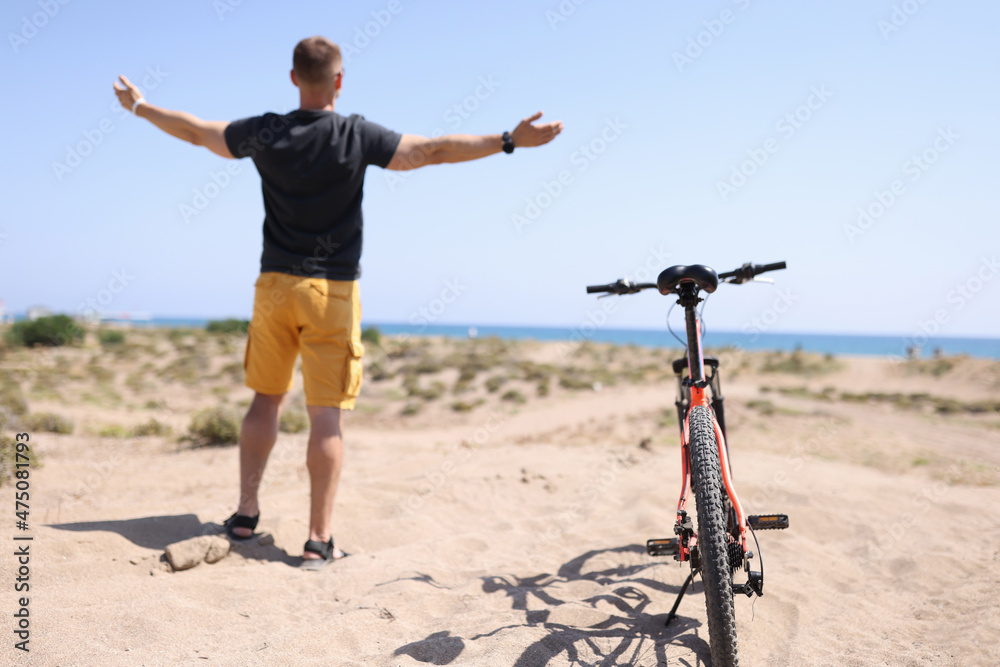 Man standing on beach near bicycle with his arms wide apart back view Man standing on beach near bicycle with his arms wide apart back view