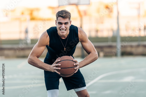 Man posing with aggressive expression while holding a basketball outdoors