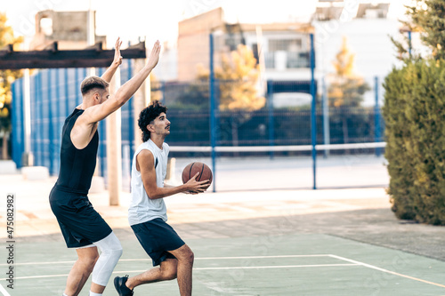 Two caucasian friends playing basketball in an outdoors court during summer