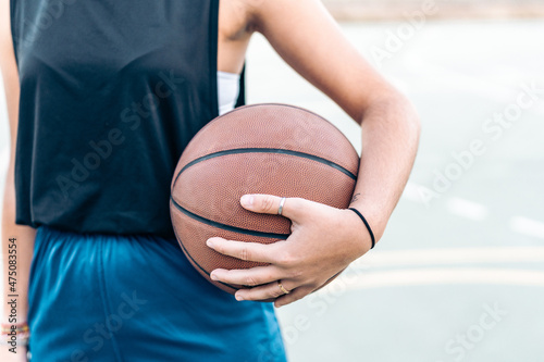 Cropped photo of a woman holding a basketball in her hand outdoors © Samuel Perales