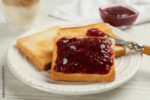 Toast with tasty raspberry jam and roasted slices of bread on white wooden table, closeup