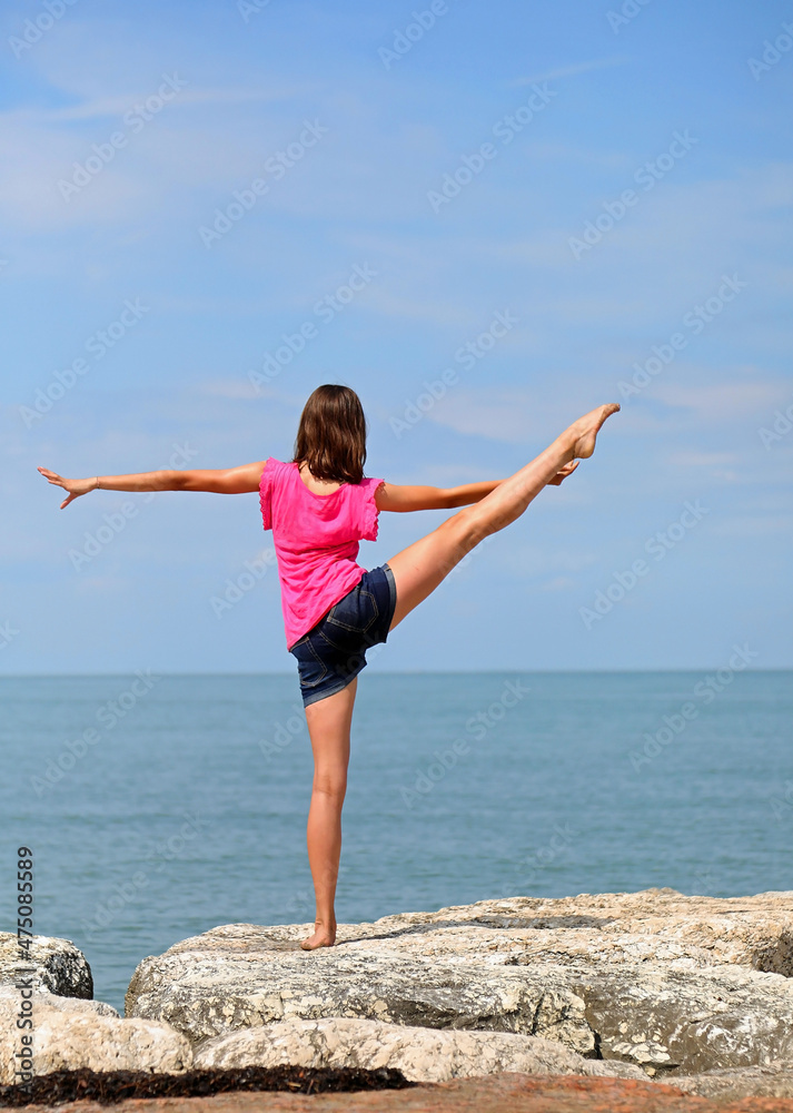 young girl with brown hair and shorts performing gymnastics exercises by the sea in the summer