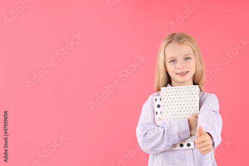 Cute little girl with notebooks on pink background