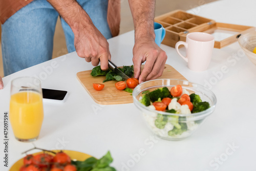 Cropped view of man cutting vegetables near smartphone and orange juice at home