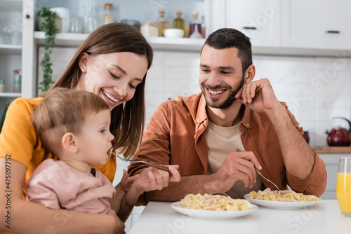 Smiling man looking at wife feeding son with pasta near orange juice in kitchen