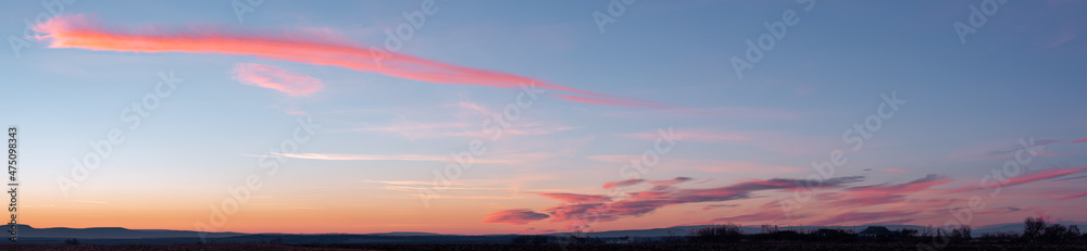 Fototapeta premium Panorama of dramatic colorful sunset with dark and bright clouds. The sun's rays are breaking through the cloudy sky. Dark clouds against a bright saturated sky.