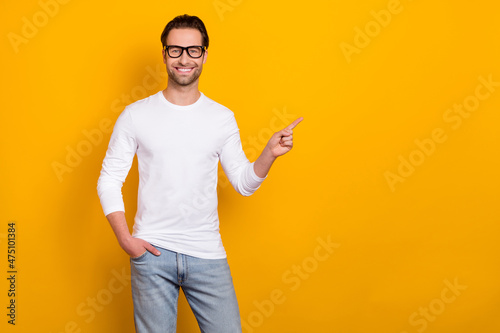Photo of optimistic brunet millennial guy index empty space wear eyewear white outfit isolated on vibrant yellow color background photo