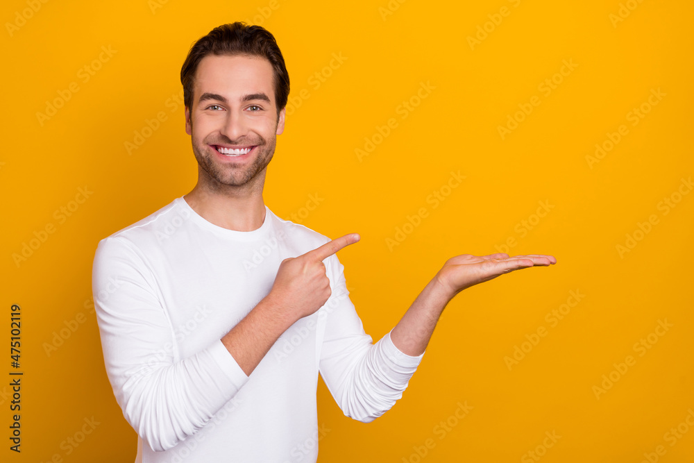 Portrait of cheerful candid person direct finger arm palm hold empty space isolated on yellow color background