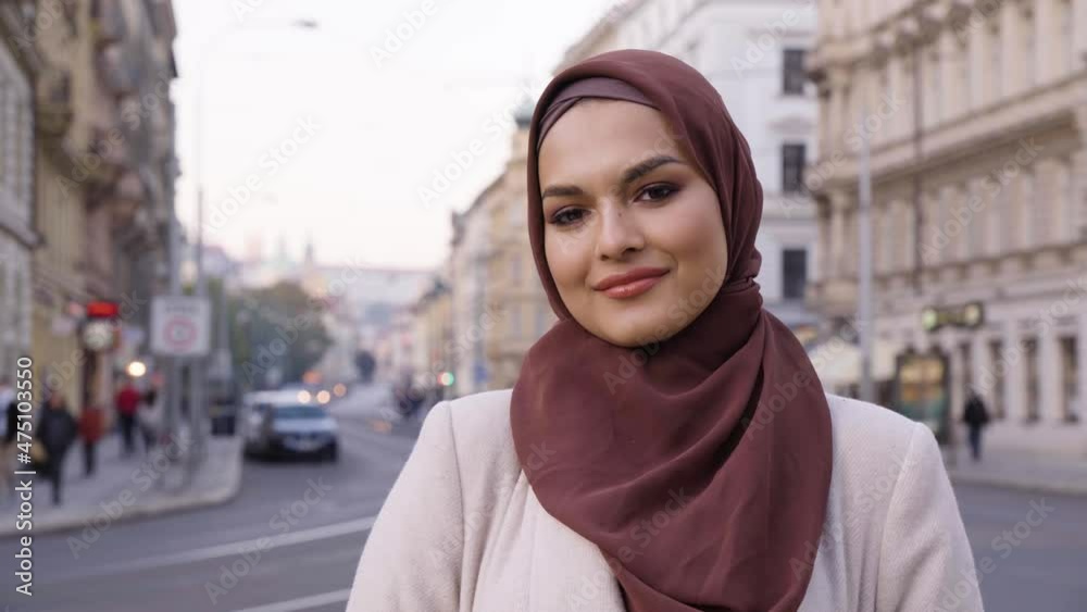 A young beautiful Muslim woman smiles at the camera in a street in an urban area - a road in the blurry background - closeup A young beautiful Muslim woman smiles at the camera in a street in an urban area - a road in the blurry background - closeup