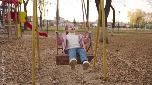 A little cheerful child swinging on a swing in an autumn park, a happy family, a kid soars high in the air, playing a game outdoors on playground, baby girl walks in the park and smiles, children joy