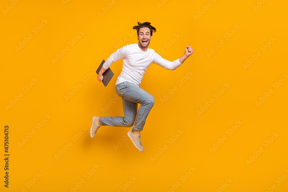 Full size photo of hooray brunet millennial guy run with laptop wear shirt jeans sneakers isolated on yellow background