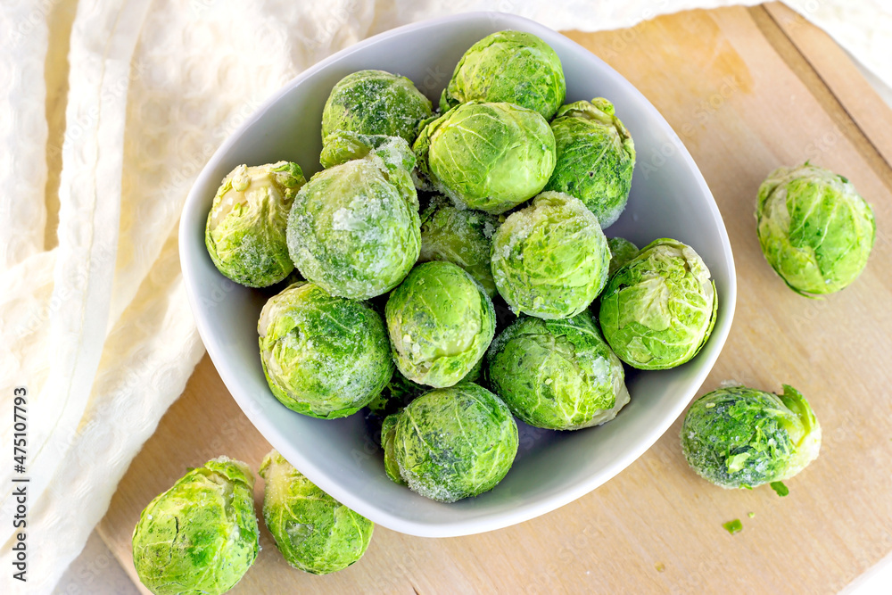 Top view of many frozen whole brussels sprouts in white bowl on light wooden background. Top view of many frozen whole brussels sprouts in white bowl on light wooden background.